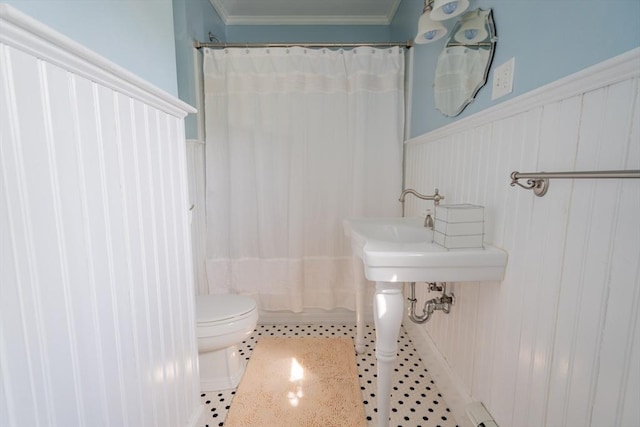 bathroom featuring crown molding, toilet, wainscoting, and a decorative wall
