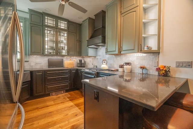 kitchen with ceiling fan, light wood-style floors, freestanding refrigerator, a peninsula, and custom range hood