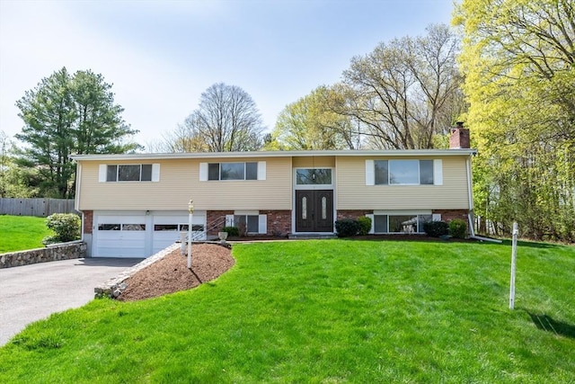 raised ranch featuring aphalt driveway, a chimney, fence, a front lawn, and an attached garage