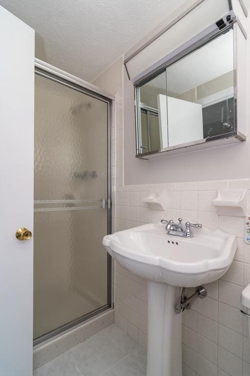 bathroom with tile patterned floors, a textured ceiling, tile walls, and a shower stall