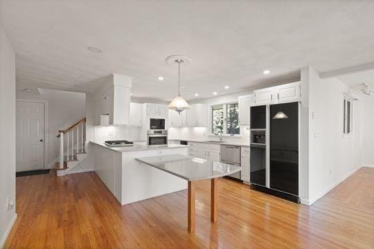 kitchen featuring black appliances, a peninsula, light wood-type flooring, white cabinetry, and hanging light fixtures