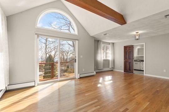 spare room with a baseboard radiator, healthy amount of natural light, high vaulted ceiling, wood finished floors, and beam ceiling
