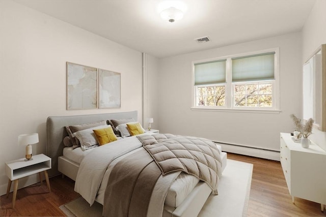 bedroom with baseboard heating and wood finished floors