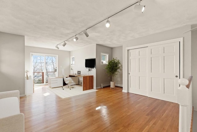 unfurnished living room featuring rail lighting, a desk, light wood-style flooring, and baseboards