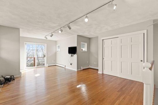 unfurnished living room featuring track lighting, a baseboard heating unit, and wood finished floors
