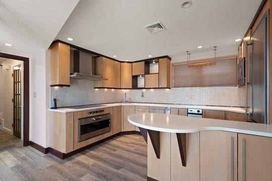 kitchen with wall oven, wall chimney range hood, open shelves, light countertops, and light wood-type flooring
