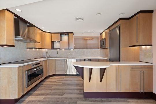 kitchen featuring stainless steel appliances, wall chimney exhaust hood, a peninsula, light countertops, and decorative backsplash