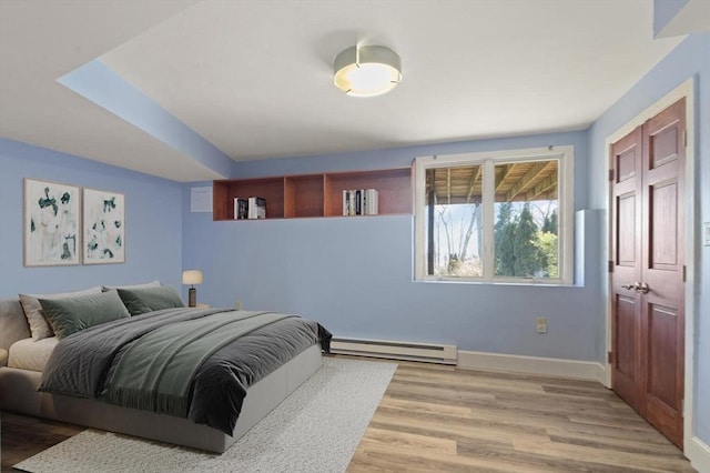 bedroom featuring a baseboard heating unit, light wood finished floors, and baseboards
