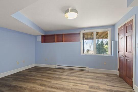 unfurnished room featuring baseboard heating, wood finished floors, and baseboards