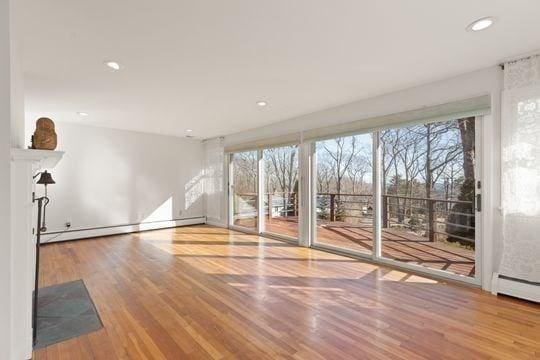 unfurnished living room featuring baseboard heating, wood finished floors, plenty of natural light, and recessed lighting