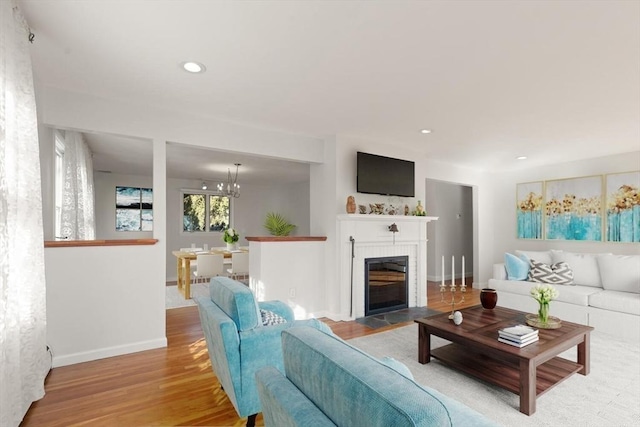 living area featuring a tile fireplace, wood finished floors, baseboards, recessed lighting, and a chandelier