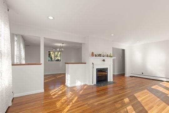 unfurnished living room featuring a baseboard radiator, wood finished floors, a fireplace with flush hearth, recessed lighting, and baseboards