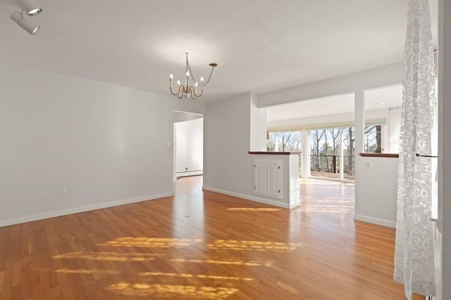 spare room with baseboards, wood finished floors, a chandelier, and a baseboard heating unit