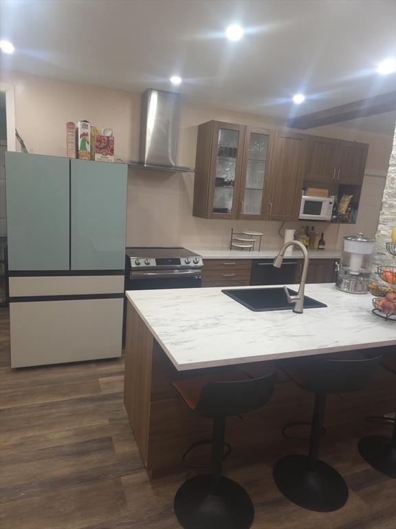 kitchen featuring sink, a kitchen bar, dark wood-type flooring, wall chimney range hood, and white appliances