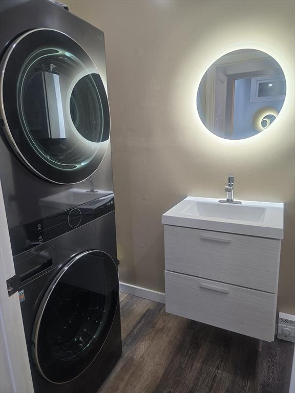 laundry room with a baseboard radiator, stacked washing maching and dryer, dark hardwood / wood-style flooring, and sink