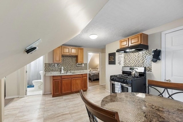 kitchen featuring stainless steel range with gas cooktop, sink, decorative backsplash, and a textured ceiling