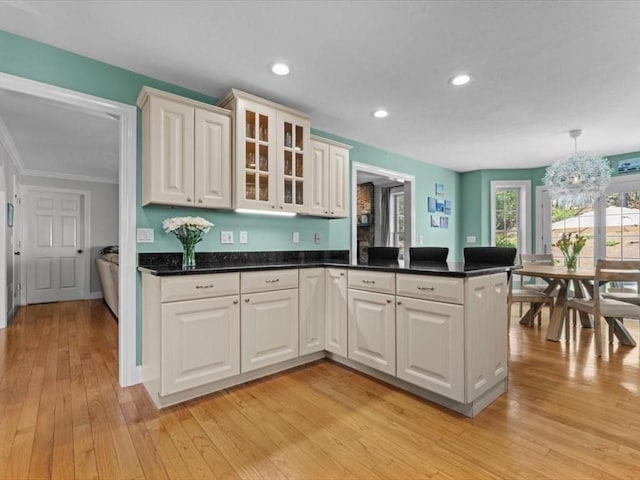 kitchen with a peninsula, light wood-style flooring, dark countertops, recessed lighting, and glass insert cabinets