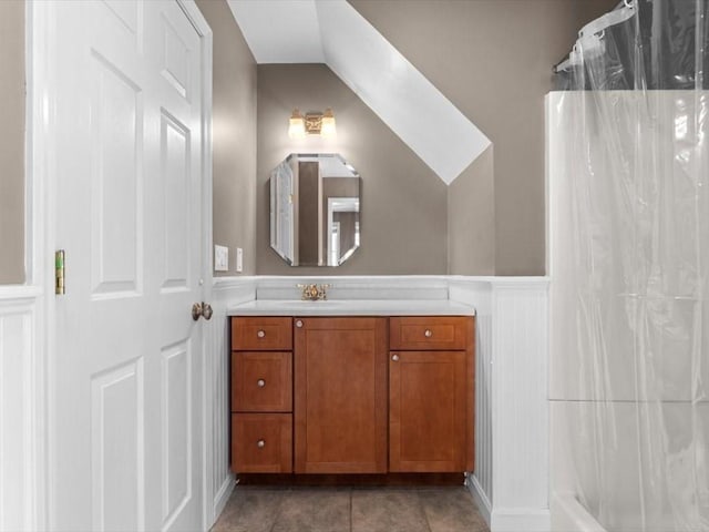 full bath with lofted ceiling, a shower with curtain, vanity, tile patterned flooring, and a decorative wall