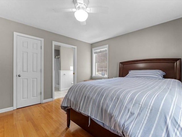 bedroom featuring baseboards, light wood-style floors, ensuite bath, and a ceiling fan
