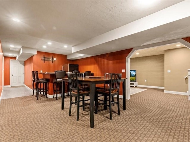 dining area featuring baseboards, light carpet, recessed lighting, bar, and wooden walls