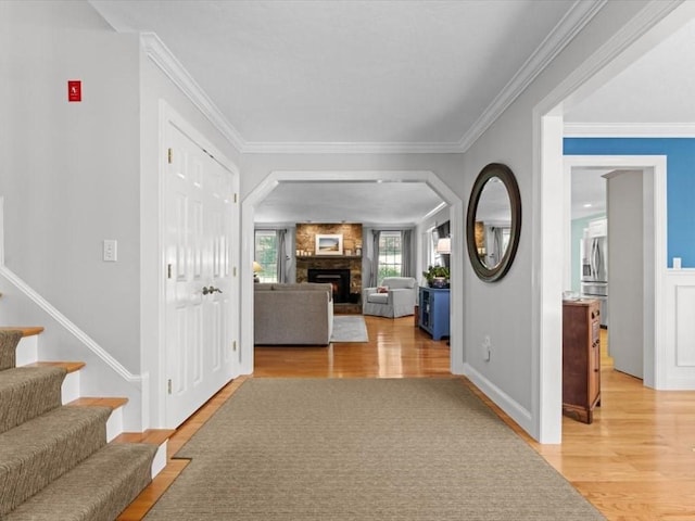 foyer entrance with light wood-style flooring, a fireplace, stairs, and crown molding