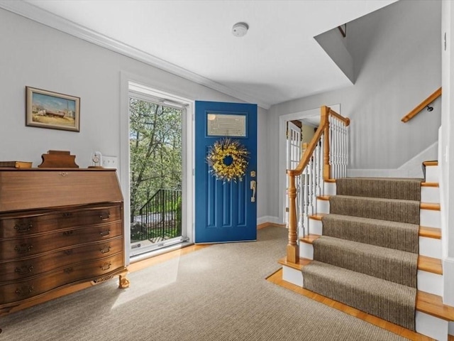 carpeted foyer featuring stairs, baseboards, and crown molding
