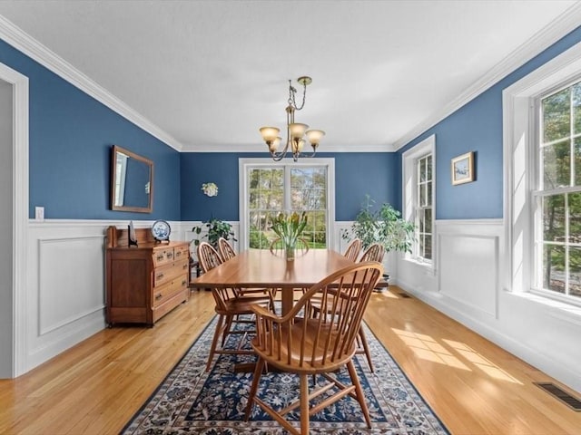 dining space featuring a chandelier, light wood-style flooring, wainscoting, and ornamental molding
