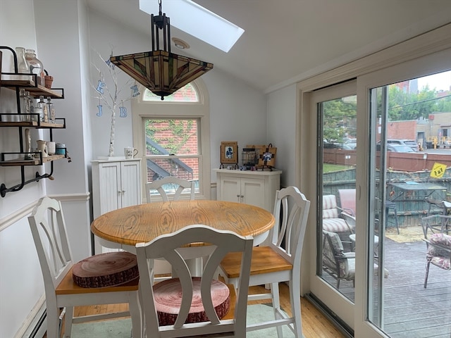 dining space featuring light wood-type flooring, vaulted ceiling with skylight, baseboard heating, and a wealth of natural light