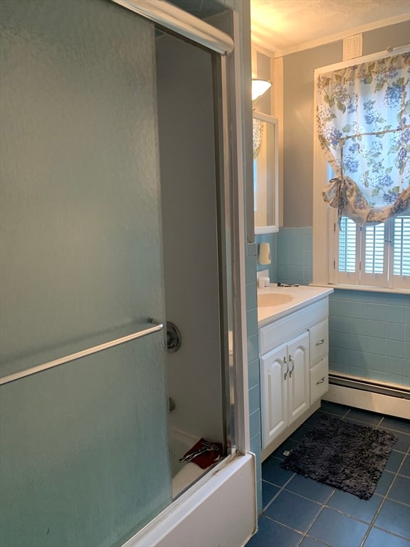 bathroom with vanity, combined bath / shower with glass door, a baseboard radiator, tile walls, and tile patterned flooring