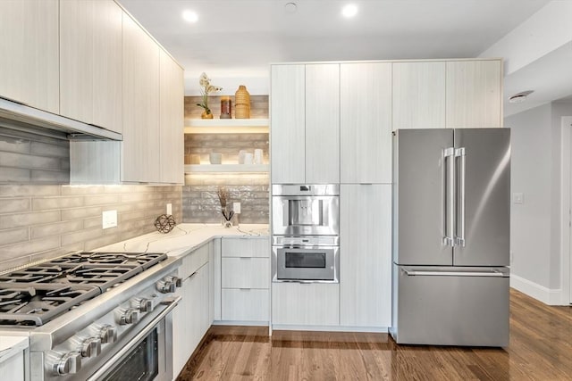 kitchen with high quality appliances, wood-type flooring, light stone countertops, and backsplash