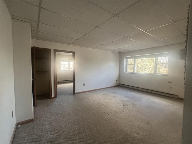 carpeted empty room with a baseboard radiator and a drop ceiling