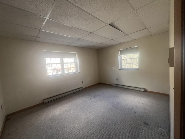 empty room featuring a drop ceiling, a healthy amount of sunlight, and baseboard heating