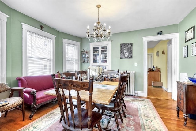 dining space with a notable chandelier, wood-type flooring, and radiator