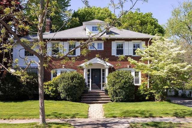 view of front of home with a chimney, a front yard, and brick siding
