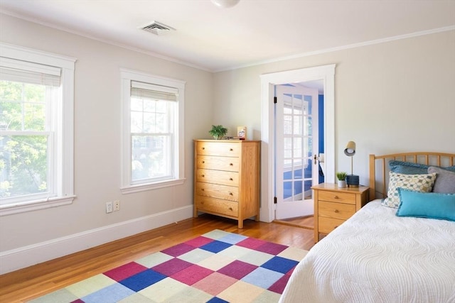 bedroom with multiple windows, light wood finished floors, crown molding, and baseboards