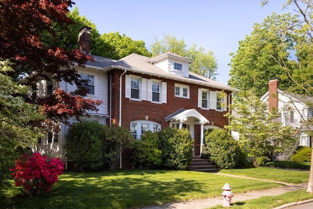 view of front of home with brick siding, a front lawn, and a chimney