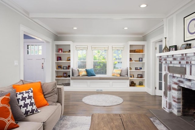 sitting room with a brick fireplace, wood finished floors, crown molding, and built in features