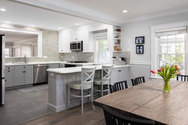 kitchen featuring appliances with stainless steel finishes, a peninsula, crown molding, tasteful backsplash, and gray cabinets