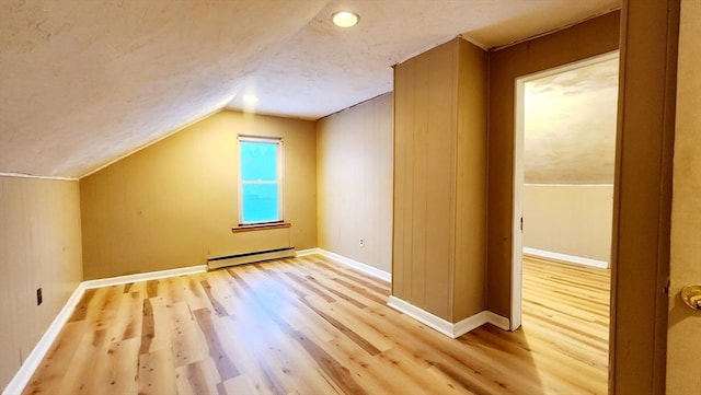 additional living space with a baseboard radiator, lofted ceiling, and light wood-type flooring