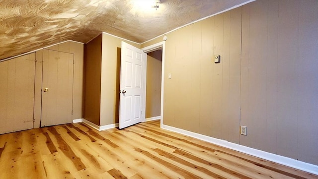 additional living space with light wood-type flooring, vaulted ceiling, and wooden walls