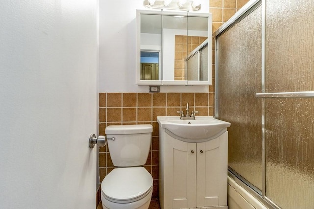 full bathroom featuring bath / shower combo with glass door, toilet, vanity, and tile walls