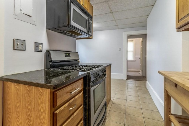 kitchen with stainless steel range with gas stovetop, dark stone countertops, a paneled ceiling, and light tile patterned floors