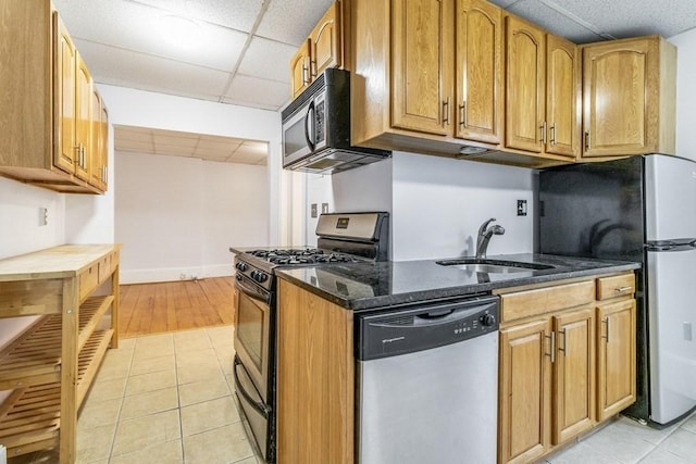 kitchen featuring light tile patterned floors, a drop ceiling, sink, dark stone countertops, and stainless steel appliances