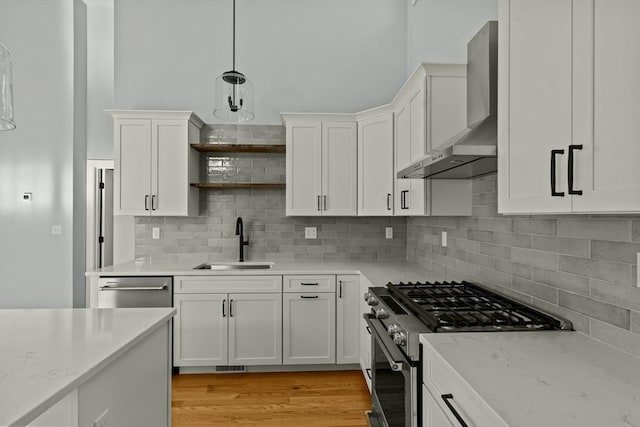 kitchen featuring wall chimney range hood, sink, appliances with stainless steel finishes, white cabinetry, and hanging light fixtures