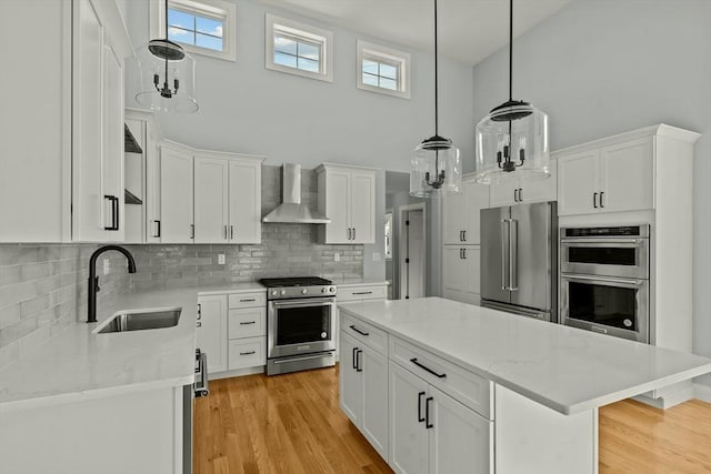 kitchen featuring sink, appliances with stainless steel finishes, white cabinets, a kitchen island, and wall chimney exhaust hood