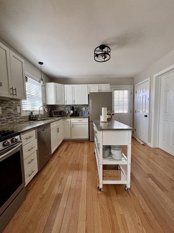 kitchen featuring open shelves, light wood-type flooring, decorative backsplash, stainless steel appliances, and a sink