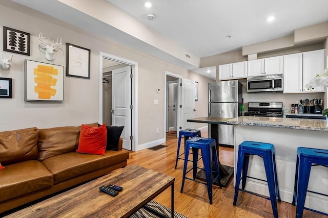 kitchen with light stone countertops, light wood-style floors, a kitchen breakfast bar, white cabinets, and appliances with stainless steel finishes