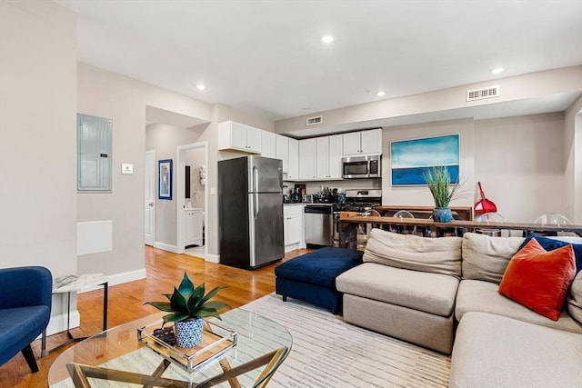 living room with recessed lighting, visible vents, light wood-type flooring, and electric panel