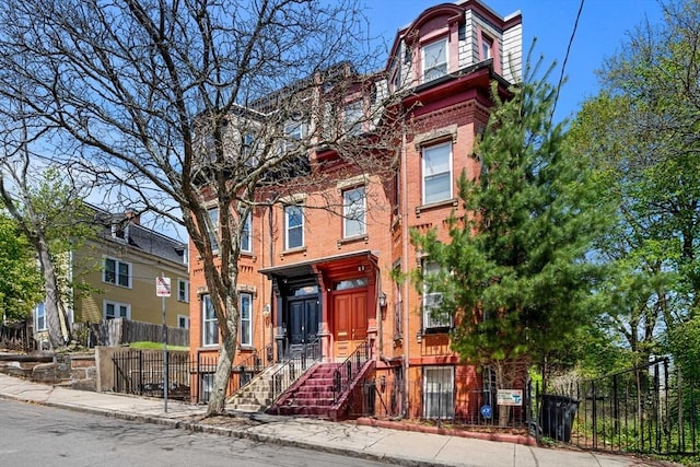 second empire-style home featuring brick siding, mansard roof, and a fenced front yard