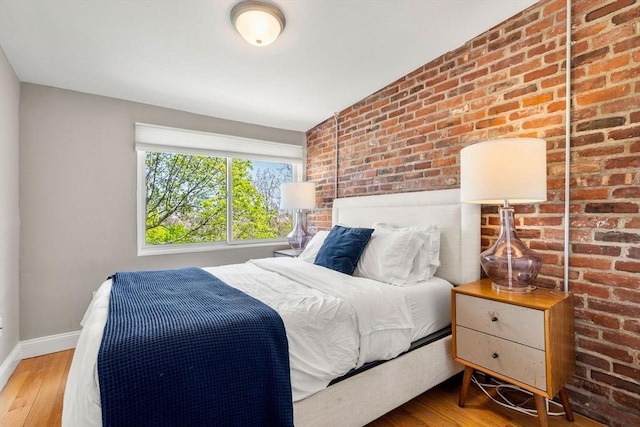 bedroom with baseboards, wood finished floors, and brick wall